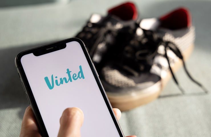 Vinted su smartphone in primo piano e scarpe usate in secondo piano