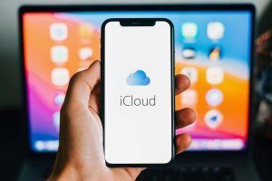 logo Apple iCloud in schermo smartphone davanti a MAC