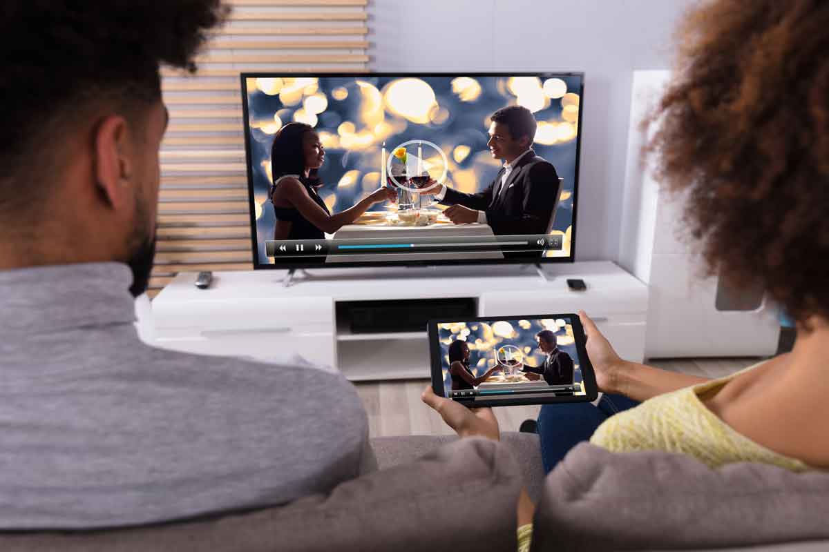 due persone mentre guardano film in streaming in tv e sul tablet
